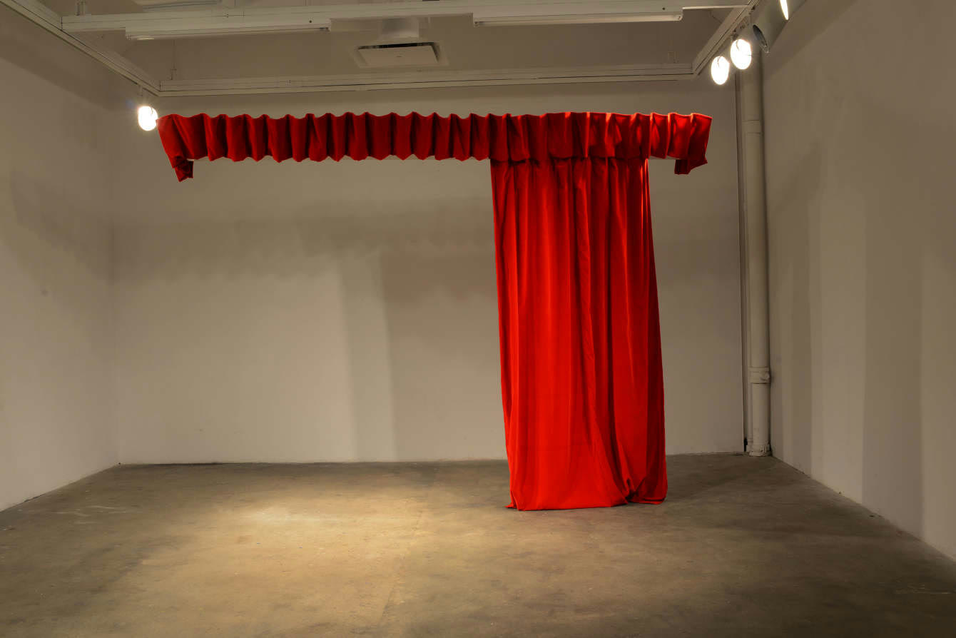A red velvet curtain hanging from a motorised track in an empty white gallery