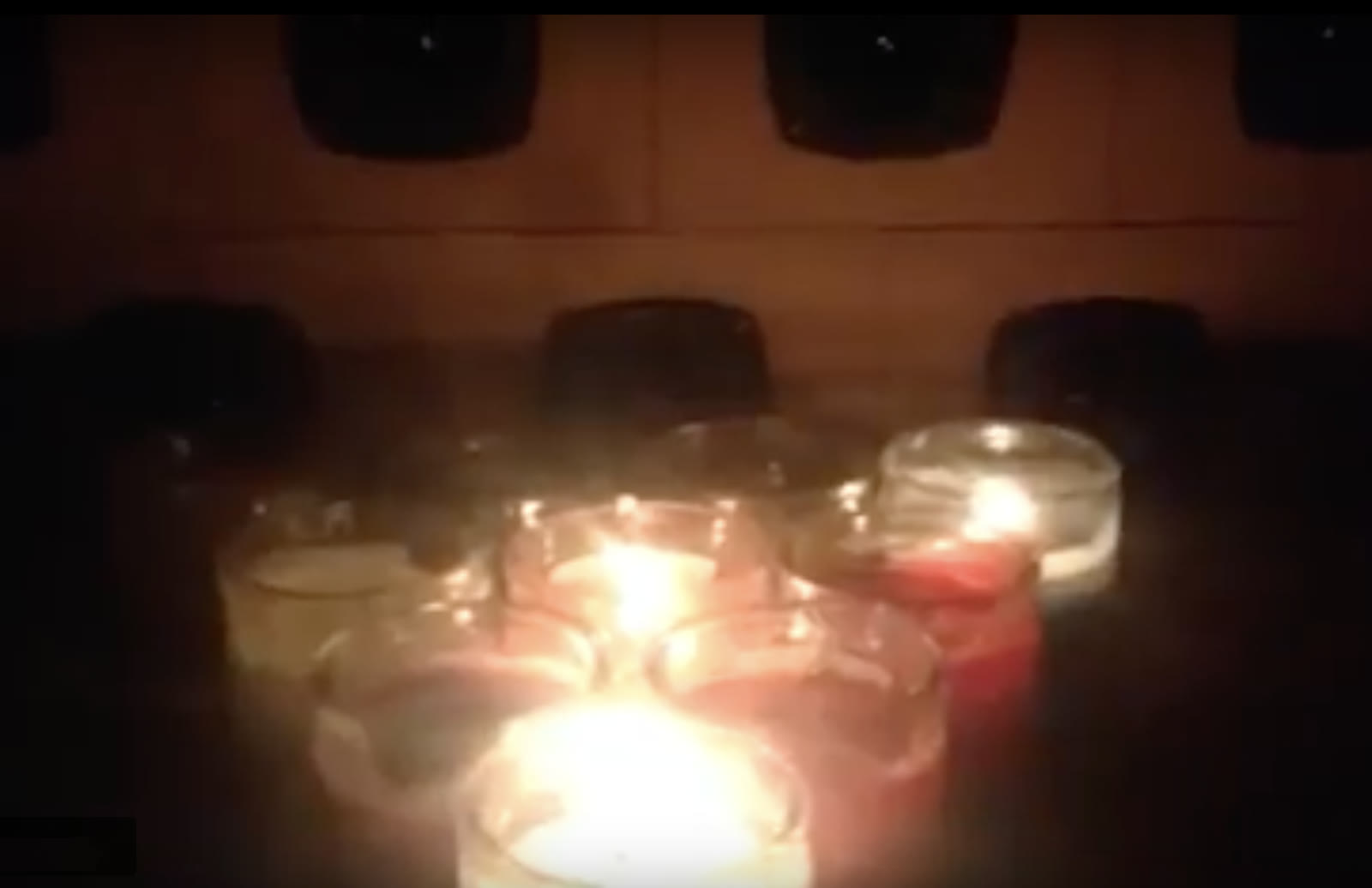 The altar in a darkened room, candlelight reflecting off the speaker cones
