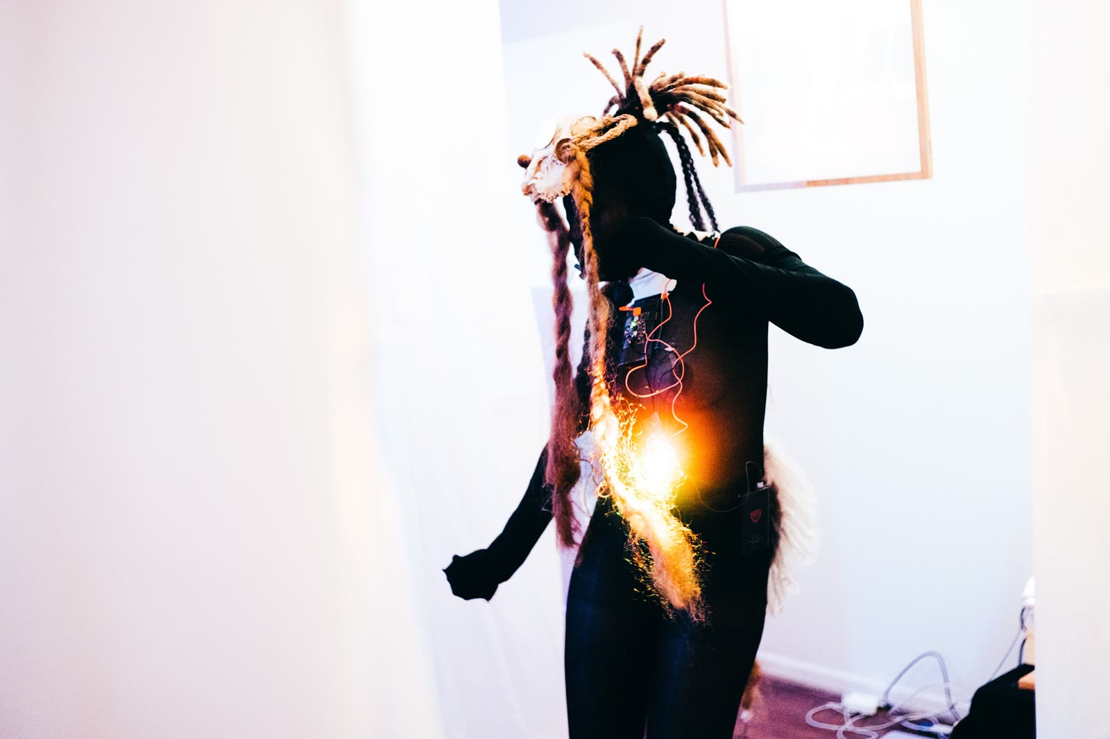 A performer in a fibre headpiece with a warm orange light glowing at the torso