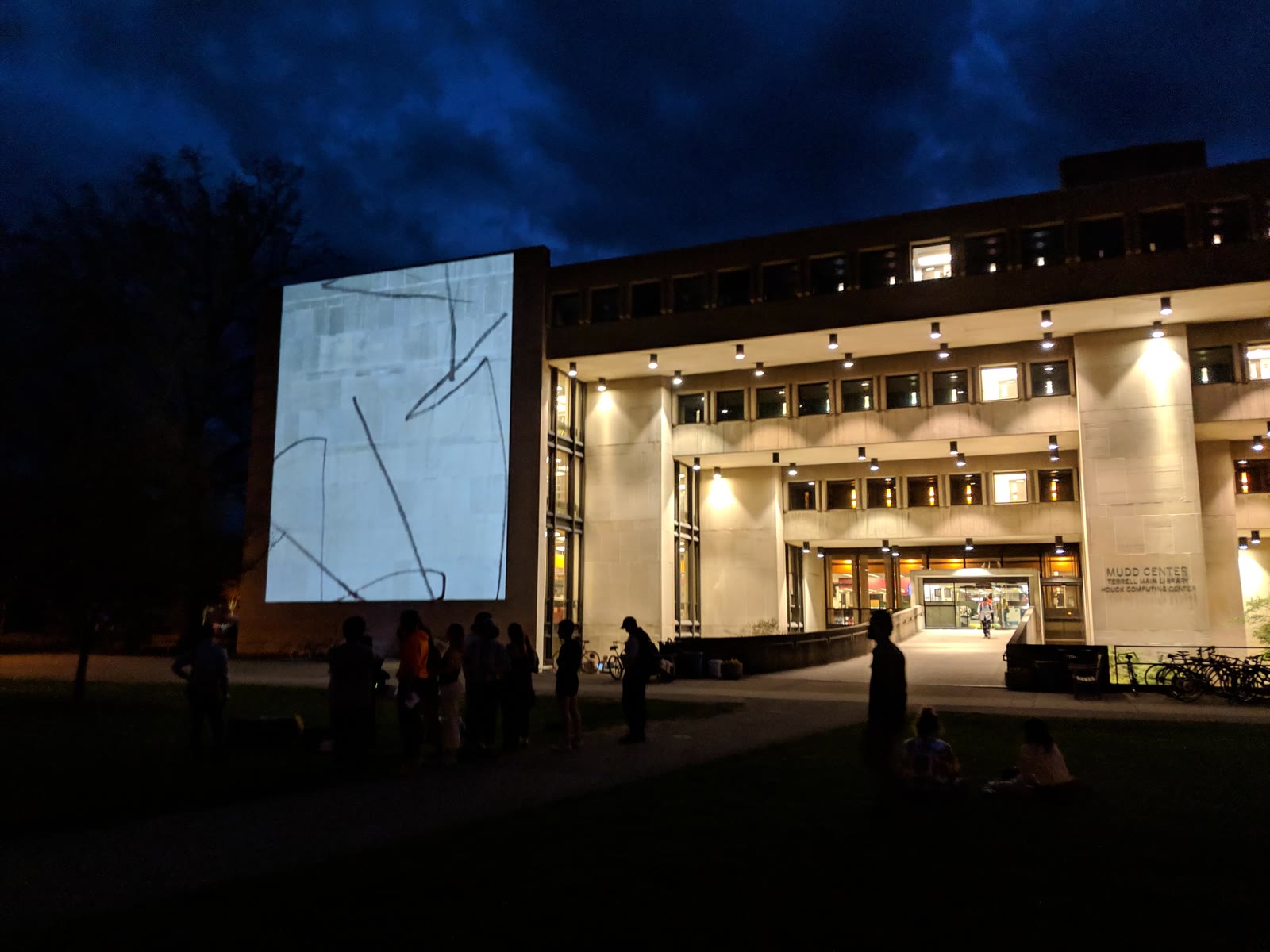 An abstract line animation projected onto the side of a library building at night while students watch