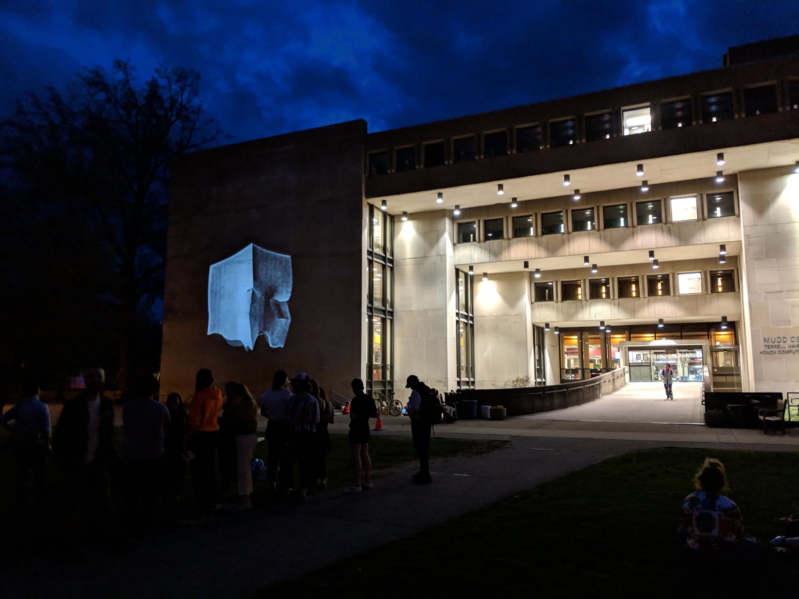 A softer luminous shape projected onto the same building facade as the crowd looks on